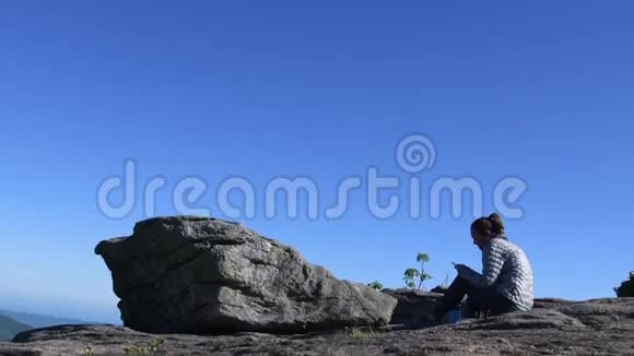 倾斜妇女在岩石上的位置和电话上的位置视频的预览图