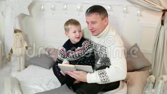 父母和一个孩子读一个故事父亲和他的小儿子一起读一本书一家人在家读书很好视频的预览图