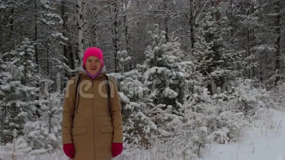 白雪皑皑的冬林中一个戴着亮粉色帽子的女孩的肖像视频的预览图