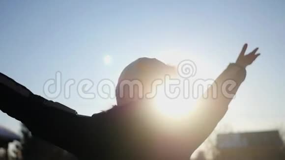 一个戴着白色帽子的女孩很高兴冬天的太阳日落举起双手捕捉镜头的效果慢慢慢慢视频的预览图