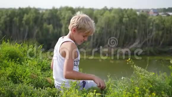 一个年轻人坐在河岸上美丽的夏日风景视频的预览图