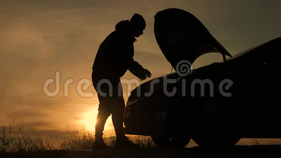 日落时剪影人正在检查那辆破车的发动机舱视频的预览图