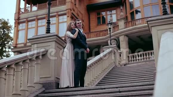 一对漂亮的宫殿附近的夫妇一个年轻人和一个穿着优雅衣服的女孩在豪宅附近的一个大楼梯上视频的预览图