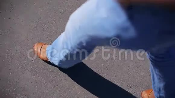 穿着蓝色牛仔裤和棕色鞋子的女孩在柏油路上散步俯瞰美景视频的预览图