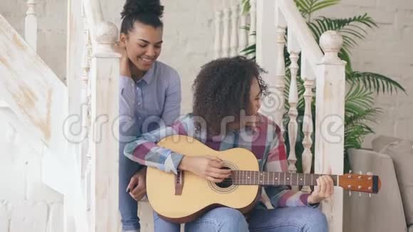 两个巴西卷发女孩坐在楼梯上练习弹吉他朋友们玩得开心唱歌视频的预览图