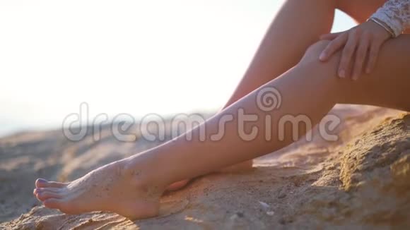 女孩在海滩上轻轻地抚摸她的腿4k视频的预览图
