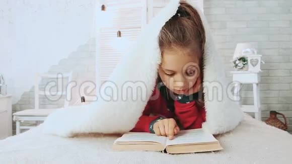 可爱的学校女孩穿着睡衣看书的肖像上面覆盖着白色的毛毯视频的预览图
