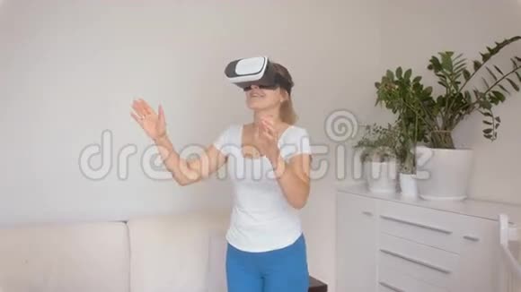 美丽的年轻女子戴着虚拟现实眼镜走在客厅里虚拟现实技术4K拍摄的录像视频的预览图