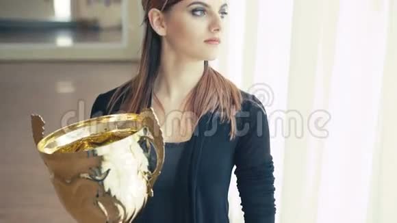 漂亮女孩的肖像带着金色的奖杯看着窗户4K视频的预览图
