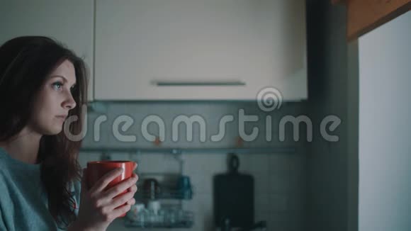 年轻的微笑女孩看着窗户早上在厨房喝咖啡视频的预览图