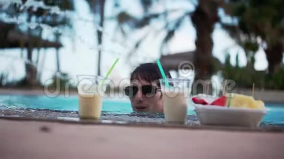 年轻的帅哥戴着太阳镜喝鸡尾酒在游泳池里放松1920x1080视频的预览图