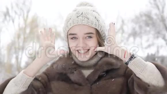 漂亮的女孩摆姿势在下雪的日子摸她的头发和冬帽慢慢地视频的预览图