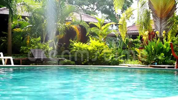 带竹平房的热带花园游泳池和棕榈树晴天带镜头耀斑的游客天堂视频的预览图