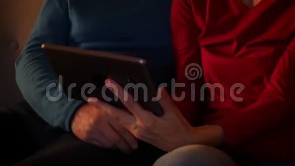 在舒适的公寓里一对老年幸福夫妇用平板电脑坐在沙发上的特写镜头视频的预览图