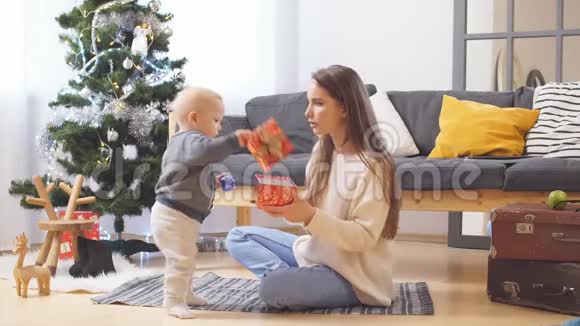 年轻快乐的家庭妈妈和小儿子在家中一起在圣诞树和新年树附近玩微笑视频的预览图