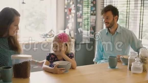 年轻的母亲和父亲正微笑着看着他们的女儿她正在早餐吃麦片粥慢点斯泰迪达姆视频的预览图