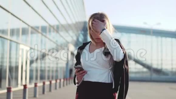 自信的性感金发女孩走在机场候机楼旁抚摸她的头发打电话给别人时尚的外观视频的预览图