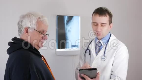 一位年轻的男医生在平板电脑上显示测试结果病人是个老人视频的预览图