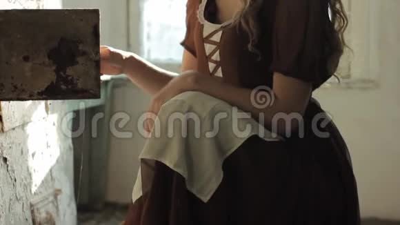 一个穿着乡村服装的女人坐在一个废弃的房子里的旧炉子旁边视频的预览图