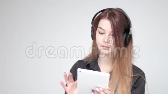 年轻漂亮的女士戴着耳机玩白色平板电脑拍照视频的预览图