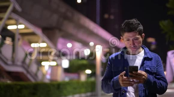 西班牙裔男子在夜间探索城市街道时使用电话视频的预览图