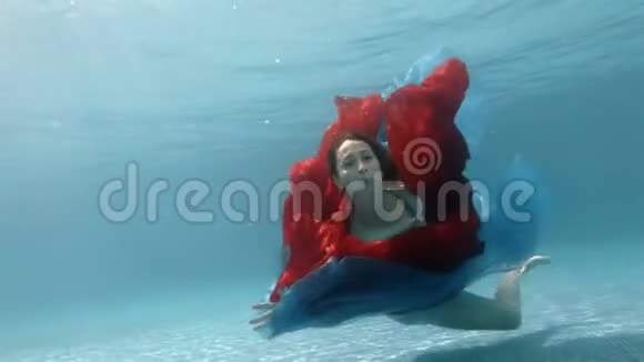 穿裙子的女孩在池底水下玩一块红布看着镜头视频的预览图