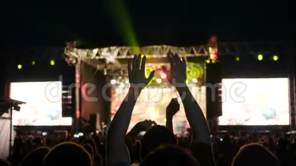 人们在摇滚音乐节上双手跳起来舞台上灯火辉煌夜间摇滚音乐会上灯火辉煌视频的预览图