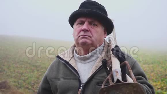 戴着帽子的老农在春田里拿着一把泥泞的锄头和鹳体力劳动福克视频的预览图