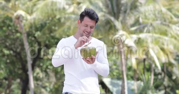 男子在棕榈树上喝椰子鸡尾酒快乐的微笑青年游客视频的预览图