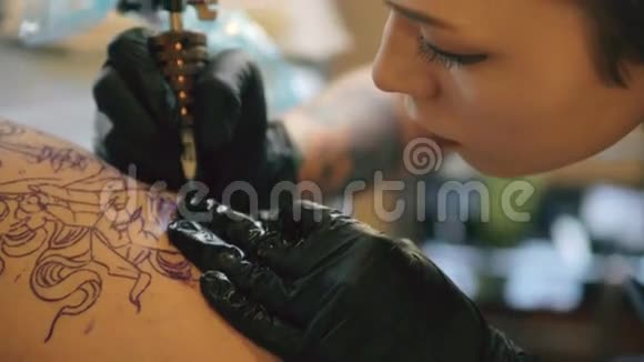 特写年轻红发纹身艺术家妇女纹身图片在客户腿上素描在工作室室内视频的预览图