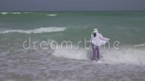 穿着衣服的少女在迪拜海滩上欢快地跳跃着波斯湾的海浪视频的预览图