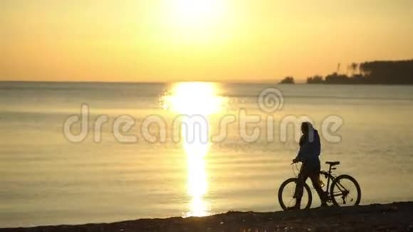日落时带着自行车的女孩沿着海滩散步浪漫的女孩视频的预览图