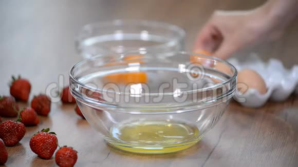 女人的手打破一个鸡蛋以分离蛋清和蛋黄和鸡蛋壳的背景视频的预览图