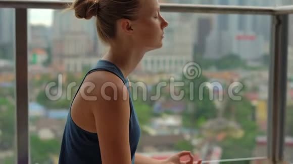 年轻女子在多层楼的阳台上做瑜伽练习可以看到一个带滑雪者的市中心视频的预览图