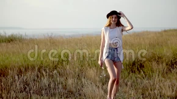 年轻漂亮的女模特戴着帽子在河边的草地上跳舞视频的预览图
