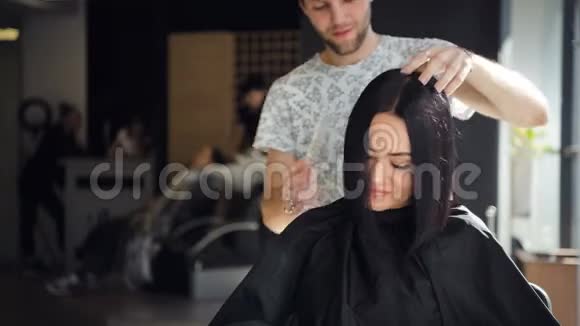 微笑发型师理发师和沙龙的客户同时为美丽的黑发女人理发视频的预览图