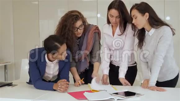 四个女人站在桌子旁边手里拿着平板电脑视频的预览图