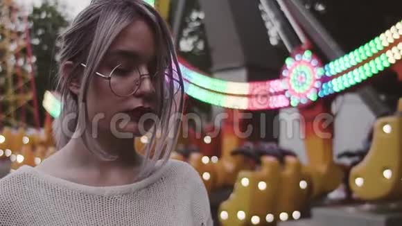 戴眼镜的嬉皮士女孩在娱乐公园的跷跷板附近抚摸头发视频的预览图