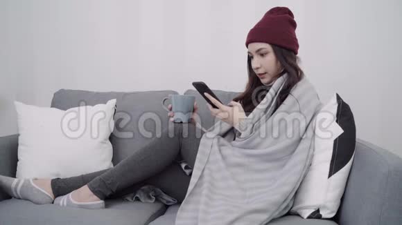美丽迷人的亚洲妇女使用智能手机发短信和阅读躺在沙发上当放松在客厅在家里视频的预览图