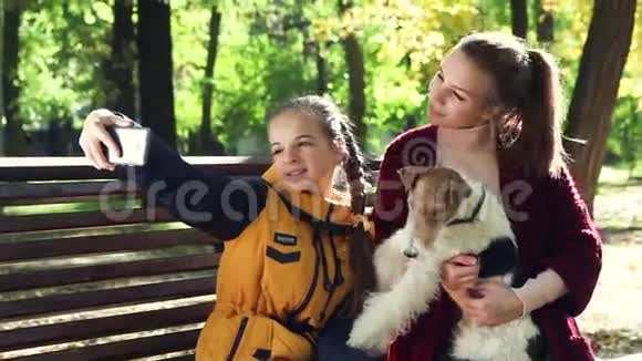 年轻迷人的女孩拥抱狗狐狸猎犬制作自拍智能手机视频的预览图