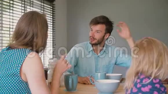 一位年轻的黑发父亲正和他美丽的妻子在厨房的桌子上交谈慢动作视频的预览图