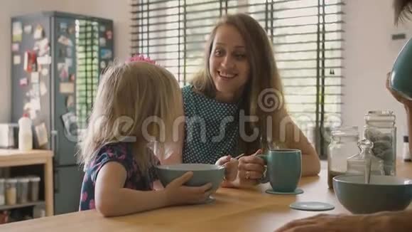 美丽的年轻母亲在早餐时和她可爱的金发女儿说话微笑着慢节奏视频的预览图