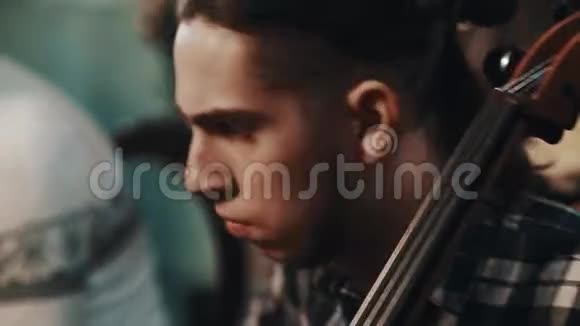 年轻的表演者扎着马尾辫穿着格子衬衫用小提琴演奏大提琴视频的预览图