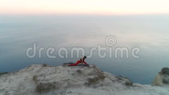 美丽的自由女子正在做瑜伽伸展在山顶与海景在日落空中镜头视频的预览图