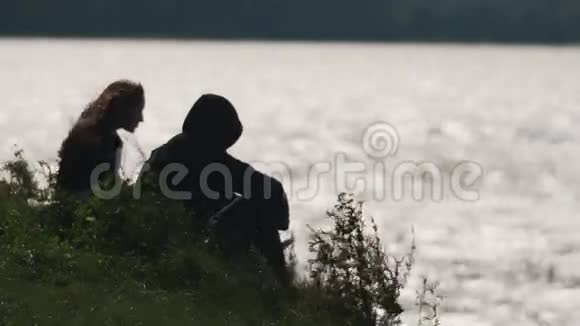 夏天刮风的时候一对夫妇坐在湖边的草地上谈话视频的预览图