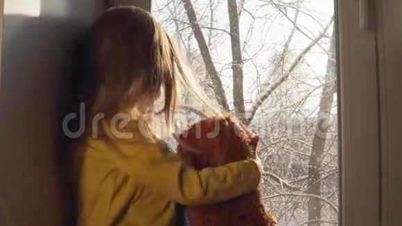 在白雪覆盖的树木背景下婴儿坐在窗台上玩耍视频的预览图