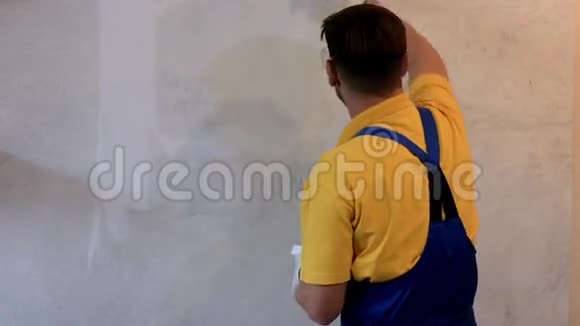 穿蓝色工作服的男画家用白色画墙视频的预览图