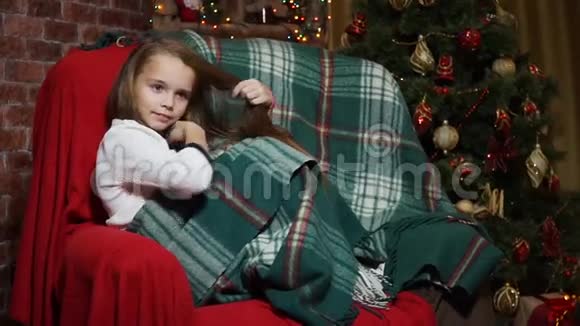女孩把头发剪直坐在圣诞树附近的椅子上视频的预览图