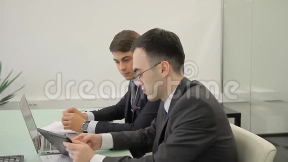 两名员工交谈坐在桌旁办公室里放着笔记本电脑和平板电脑视频的预览图