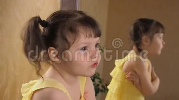 一个害羞的小女孩照镜子穿着黄色裙子的漂亮女孩对着镜子头上有尾巴的孩子视频的预览图